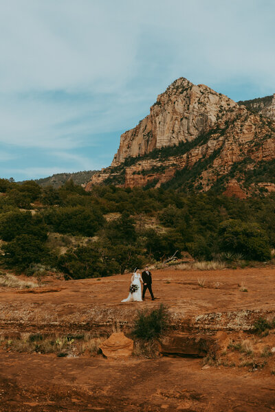 bride and groom walk within adventurous red rocks of sedona