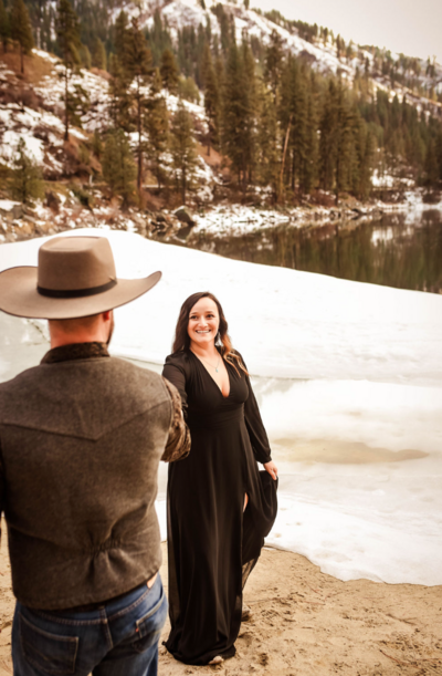 woman in a black dress and man in jeans and cowboy hat taking an engagement photo