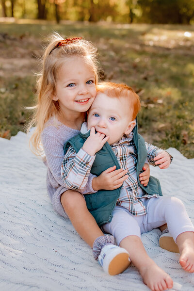 A young red haired boy and blonde haired girl sitting close together and hugging.