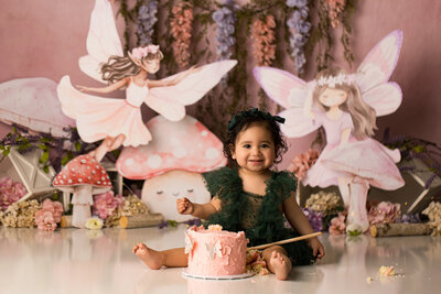 baby eating pink cake on cake smash backdrop