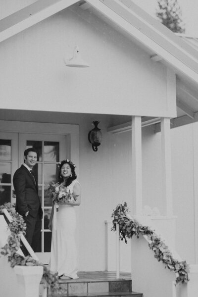 Classic black and white wedding portrait of a bride and groom in front of a small chapel