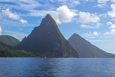 Stunning view of the Pitons in Saint Lucia, two iconic volcanic mountains rising from the lush coastline under a bright blue sky, perfect for showcasing St. Lucia travel tips with Passports & Palms Travel Co.