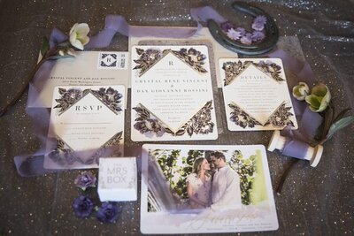 A collection of wedding stationery adorned with purple ribbon, flowers and a horse shoe detail.