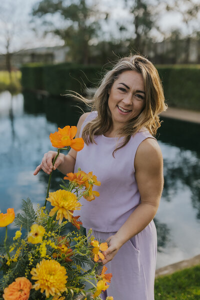 Peaches and Poppies owner headshot holding orange flowers and smiling at the camera
