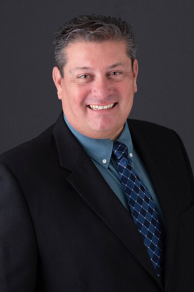 Ottawa headshot photography showing a smiling male in a blue suit  on a charcoal backdrop taken by JEMMAN Photography Commercial