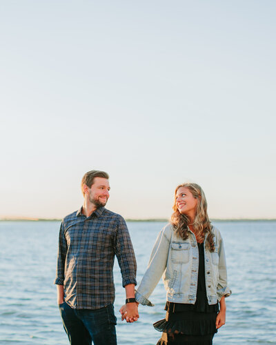 A couple holding hands and smiling at each other at the beach 