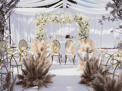 Outdoor wedding ceremony site with floral arch backdrop and luxurious drapings