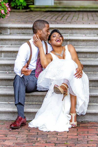 African American couple sitting on steps in front of building in wedding attire smiling and laughing