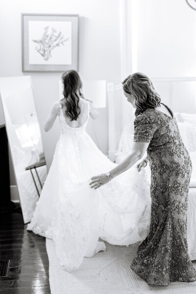 Black and white photo of bride's mom adjusting her train in front of a mirror