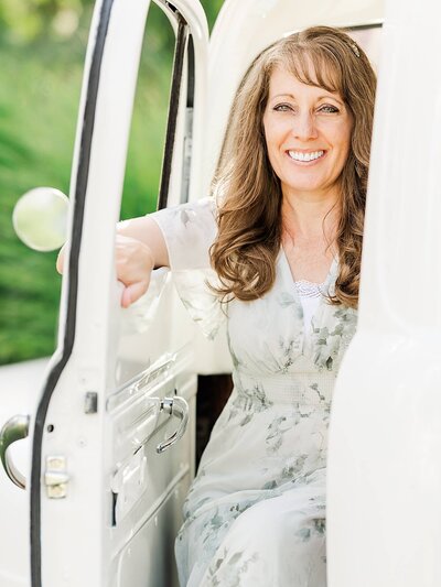 Jennifer Hall at Jennifer Hall Photography, LLC sitting outdoors in a white, vintage truck.