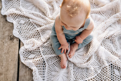 A close-up shot from above of a baby sitting on a delicate crochet blanket, bathed in warm sunlight.