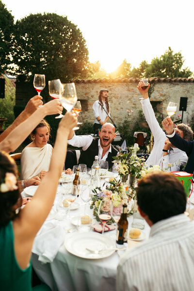 The bride and groom cheer with guests during the wedding reception, capturing a joyous moment as the sun sets, casting a warm glow over the glasses