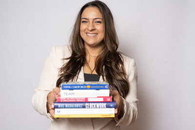 The potential with Assia Mahmood, adorned in a white blazer and surrounded by her favorite books, as she empowers successful female entrepreneurs to embrace their CEO mindset and achieve their goals.