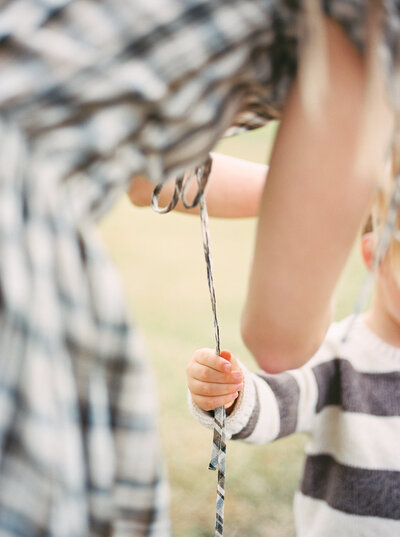 Detail film image of a boy's hands holding onto the strings of his mother's dress