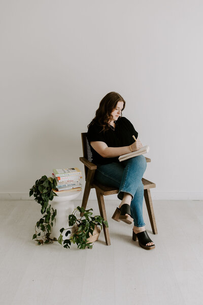 Mental health counselor takes session notes in chair next to table with books and plants