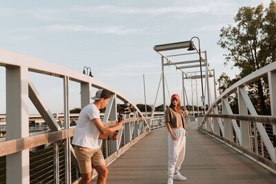 A man taking photos of a woman posing on a bridge.