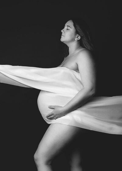 Pregnant mother in tan dress with small flowers holding baby bump outside