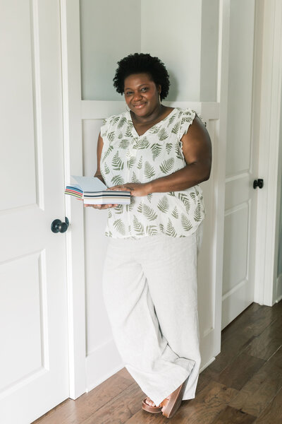 Portrait of Morgan, founder of Grey Cove Designs, standing against white paneled doors while holding custom luxury paper samples featuring high end cardstock for wedding invitations and stationery.