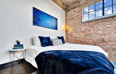 Master bedroom with exposed brick and urban fixtures in this one-bedroom, one-bathroom condo in the historic Behrens building in downtown Waco, TX
