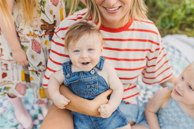 a baby wearing overalls smiling while being held by his mom