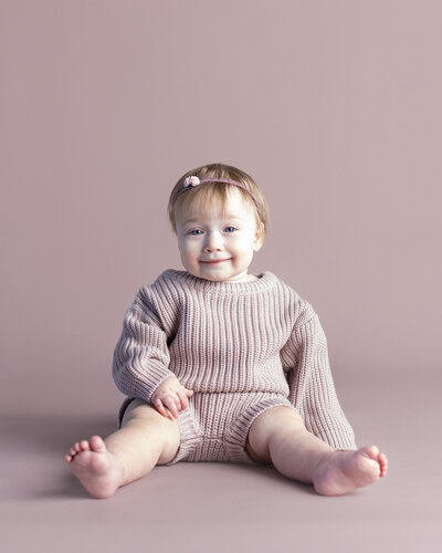 Baby girl smiles with light on her face during her first birthday milestone session.