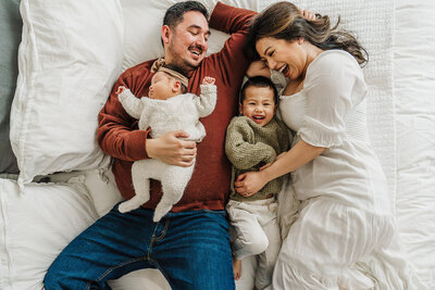 family with newborn baby lays on white bed together