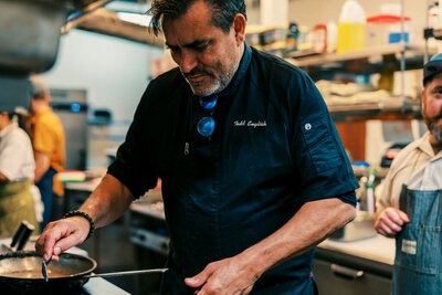 Celebrity chef Todd English preparing a dish in a professional kitchen, photographed by Joseph Mayden for culinary branding and event media coverage.