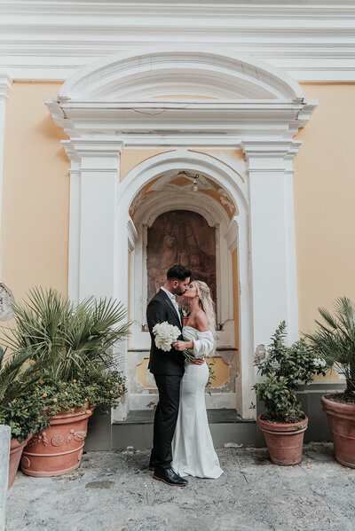 Wedding couple kiss in beautiful white Italian archway on the streets of Positano.