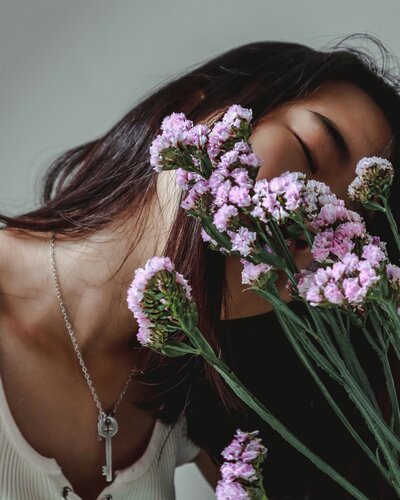 a woman holding purple flowers with her eyes closed wearing a key necklace
