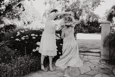 black and white image of 2 girls in dresses.  One girl is spinning the other and her hair  and skirt show the motion of the photo.