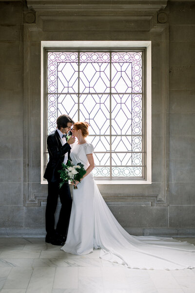 Bride and Groom Embrace by Elegant Window at Luxury California Wedding in San Fransisco City Hall