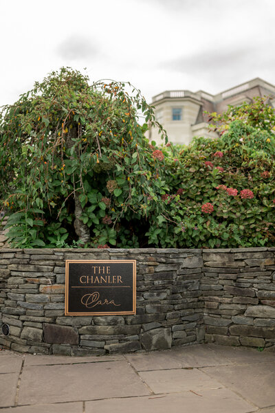 The elegant stone entrance sign for The Chanler at Cliff Walk in Newport, Rhode Island, framed by lush greenery and flowers. A luxurious seaside hotel perfect for weddings, romantic getaways, and coastal celebrations.