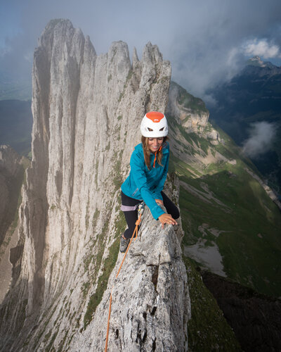 Woman in a blue coat climbing across Knife ridge in Alpstine, Switzerland