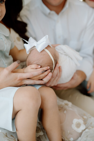 Newborn baby girl wearing white being held by sibling and parents for Newborn Photo Session.