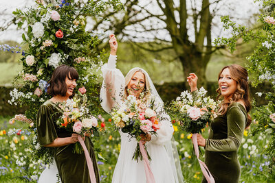 bride and groom posing with brideamaids with flowers in the air