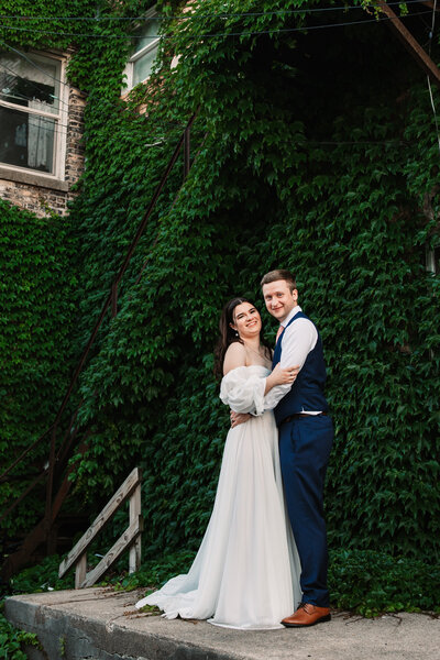 A bride and groom walk on a sidewalk with arms wrapped around each other while smiling for a Milwaukee Wedding Photographer