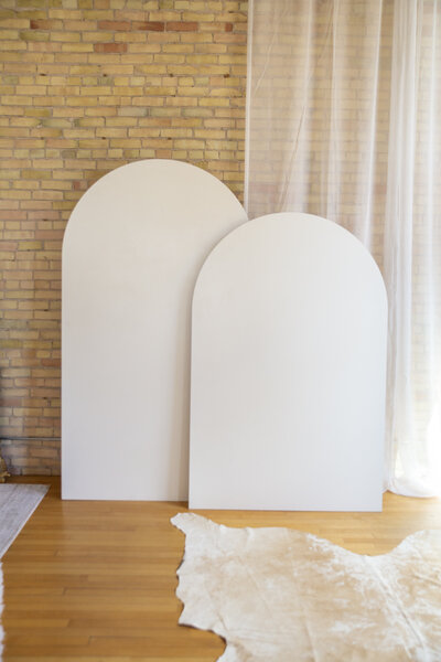 A seven foot and six foot white wooden arch backdrop against a brick wall.