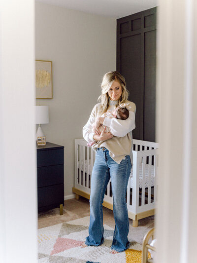 Mom holding a newborn baby in a modern nursery with a board and batten accent wall and white crib- photo by Maegan R Photography