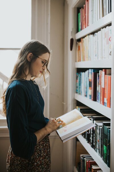 Woman standing in front of a bookshelf reading a book