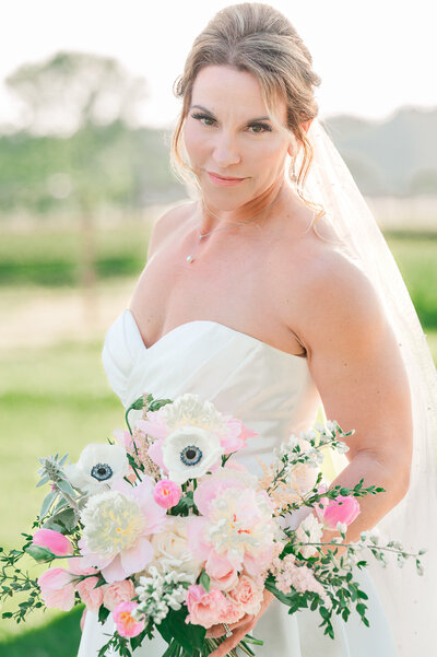 A brunette bride on her wedding day enjoying her Raleigh wedding photos at Highrock Farms while holding her wedding bouquet by JoLynn Photography