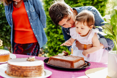 A little girl is trying to touch her first birthday cake candle and her mom is trying to stop her.