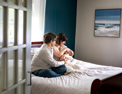 mother and father snuggling baby on bed with french door used as foreground 
