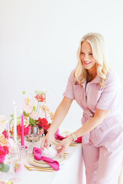 Ashley Wallace wearing a light pink jumpsuit adjusting a pink themed table setting