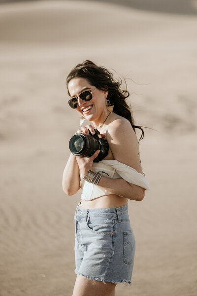 Colorado elopement photographer poses with her camera at the great sand dunes.