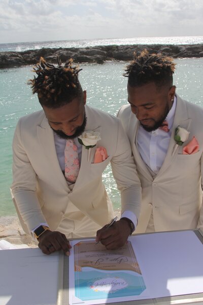 Two suited men signing a wedding book on the beach, capturing a memorable moment at their destination wedding.