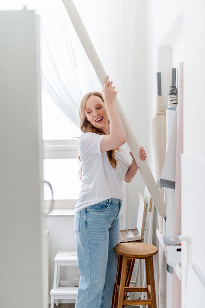 Portretfotograaf Isabeau Bosscher tilt opgerolde backdrop op in haar fotostudio en lacht.
