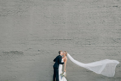 Bride and Groom hug and laugh surrounded by their bridal party. Bride has a flower crown and groom is in  a black tux. Anna Brace, a wedding photographer omaha nebraska