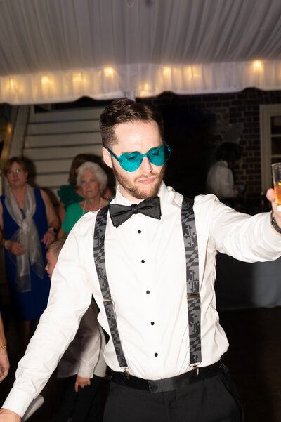 A groom dancing at a wedding reception with colored glasses on