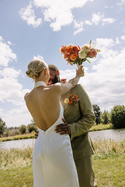 The bride and groom embrace tenderly, her bouquet cradled between them—an intimate moment framed by love, warmth, and florals in full bloom.