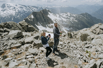 A bride and groom wearing a yellow and green puffy jacket hold each other on top of Rainbow Glacier in Whistler. There is snow all around and blue skies.